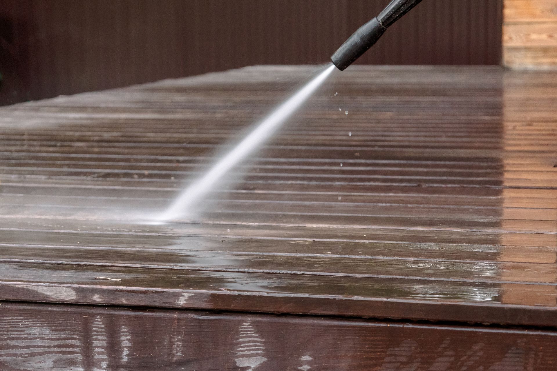 A pressure washer sprays water onto a wooden deck to clean its surface.