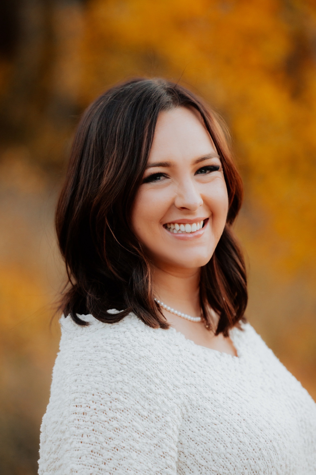 A woman wearing a white sweater and a pearl necklace is smiling for the camera.