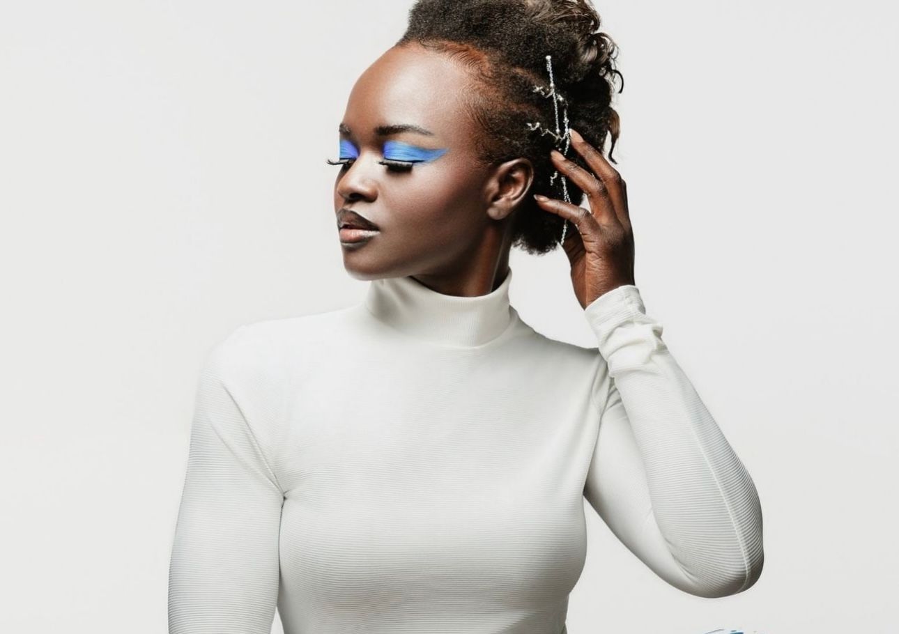Woman with blue eye makeup, white turtleneck, and textured hairstyle, looking over her shoulder.
