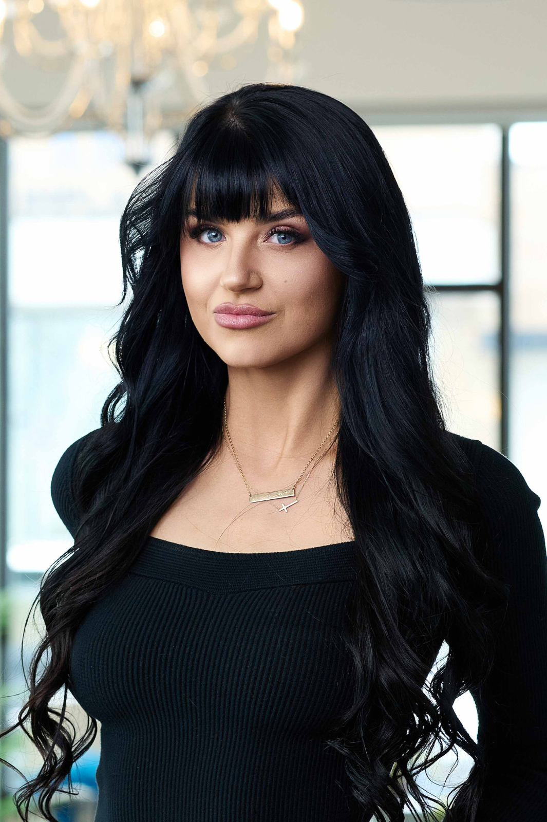 A woman with long black hair is wearing a black sweater and a necklace.
