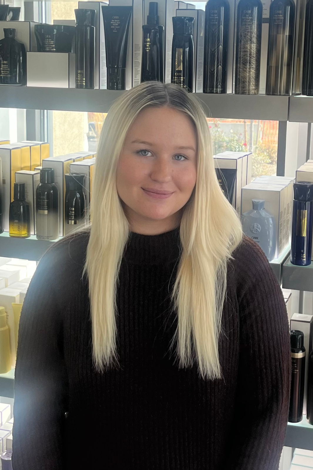 A woman is standing in front of a shelf full of hair products.