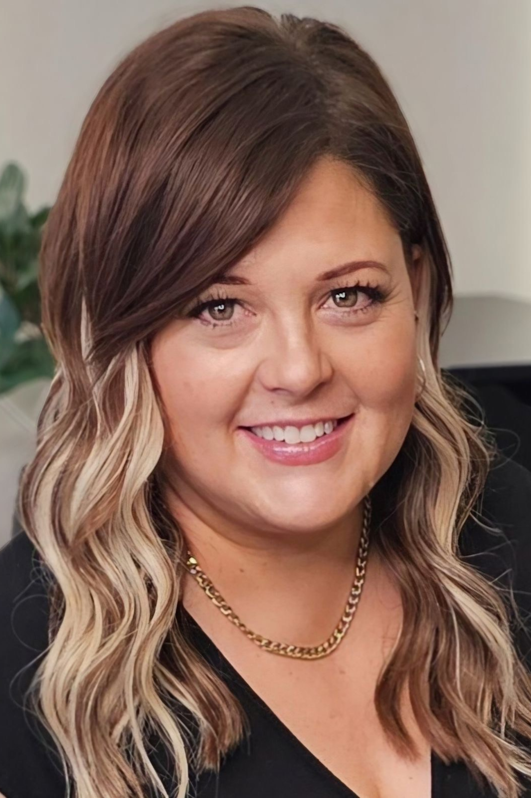 A woman wearing a black shirt and a gold necklace is smiling for the camera.