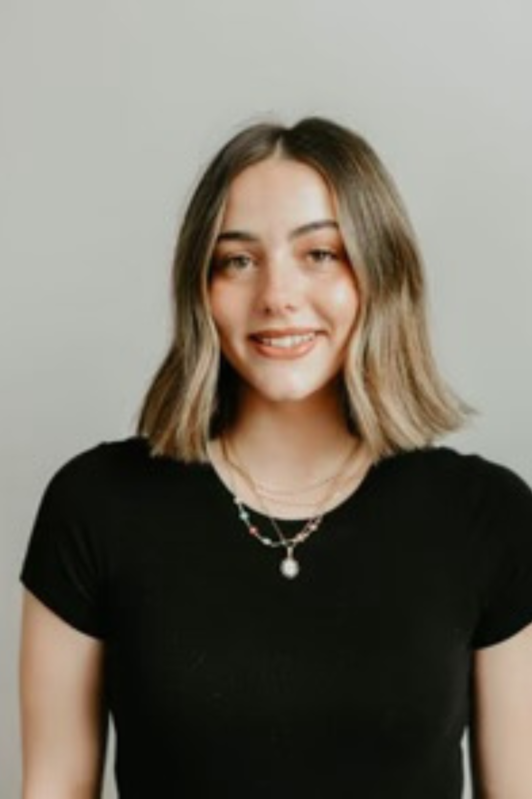 A woman wearing a black shirt and a necklace is smiling for the camera.
