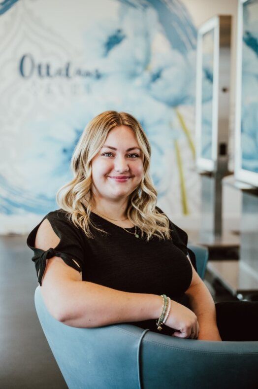 The woman is wearing a black sweater and smiling with her arms crossed.