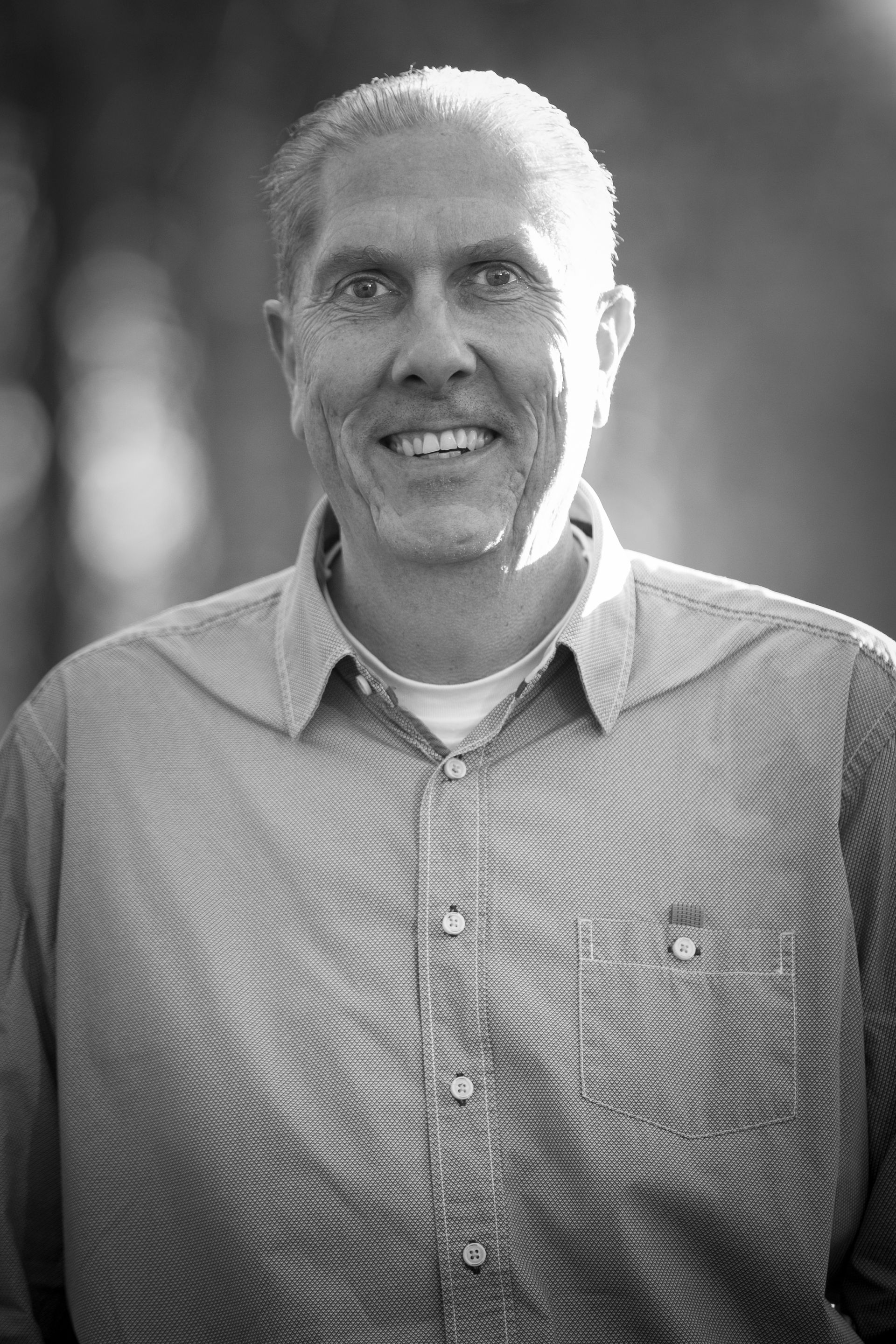 Smiling man in a button-down shirt, standing outside. Black and white photo.