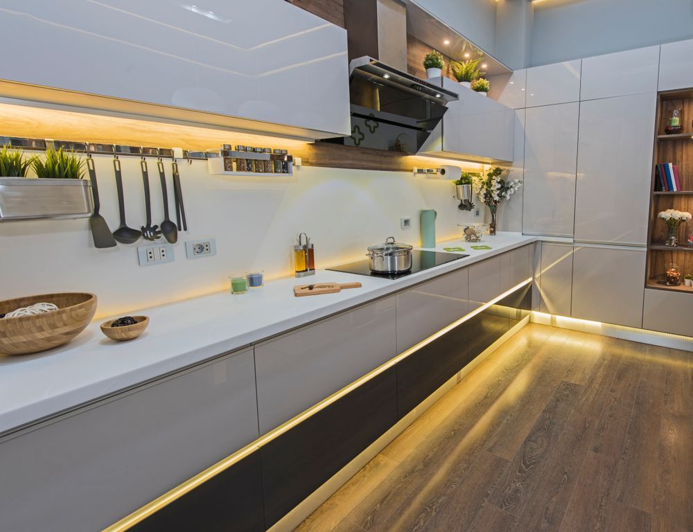 Modern kitchen with white and gray cabinets, under-cabinet and floor lighting, stainless steel appliances, and wooden floor. — Ryphen Electrical in Highton, VIC