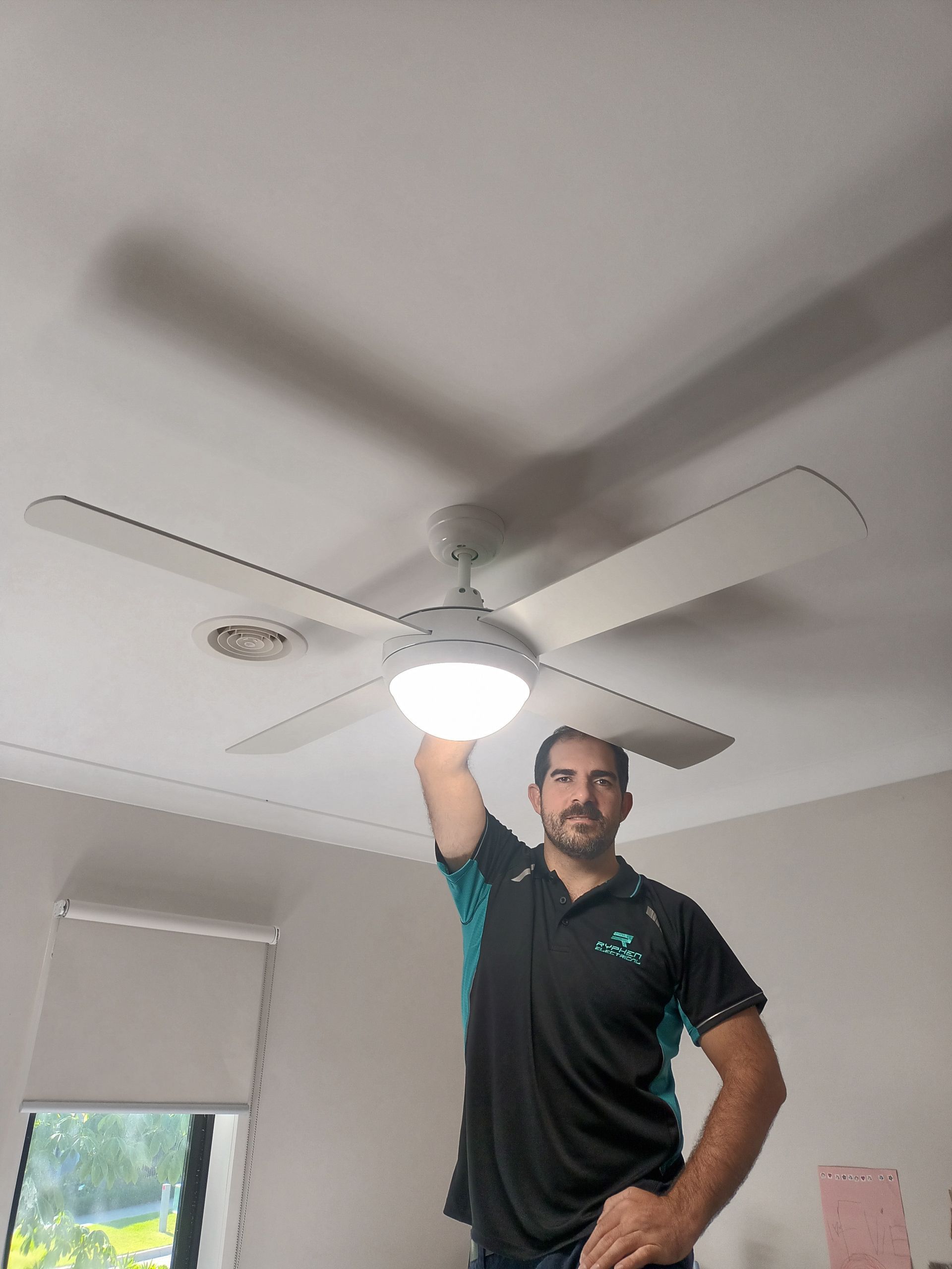 Man standing, touching a ceiling fan with light, in a room. — Ryphen Electrical in Highton, VIC