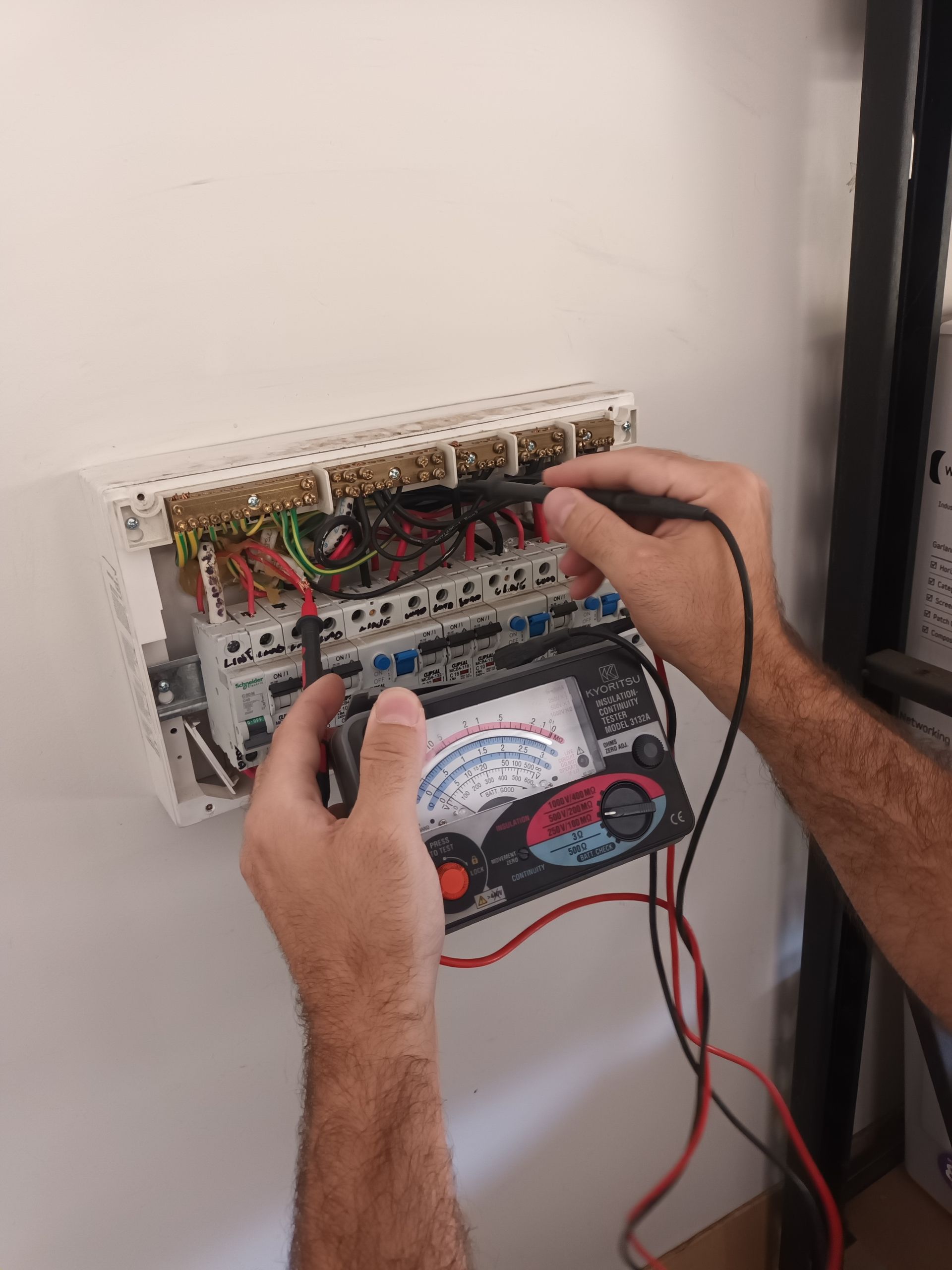 Person testing electrical panel with a multimeter. Black and red wires. White panel on a wall. — Ryphen Electrical in Highton, VIC