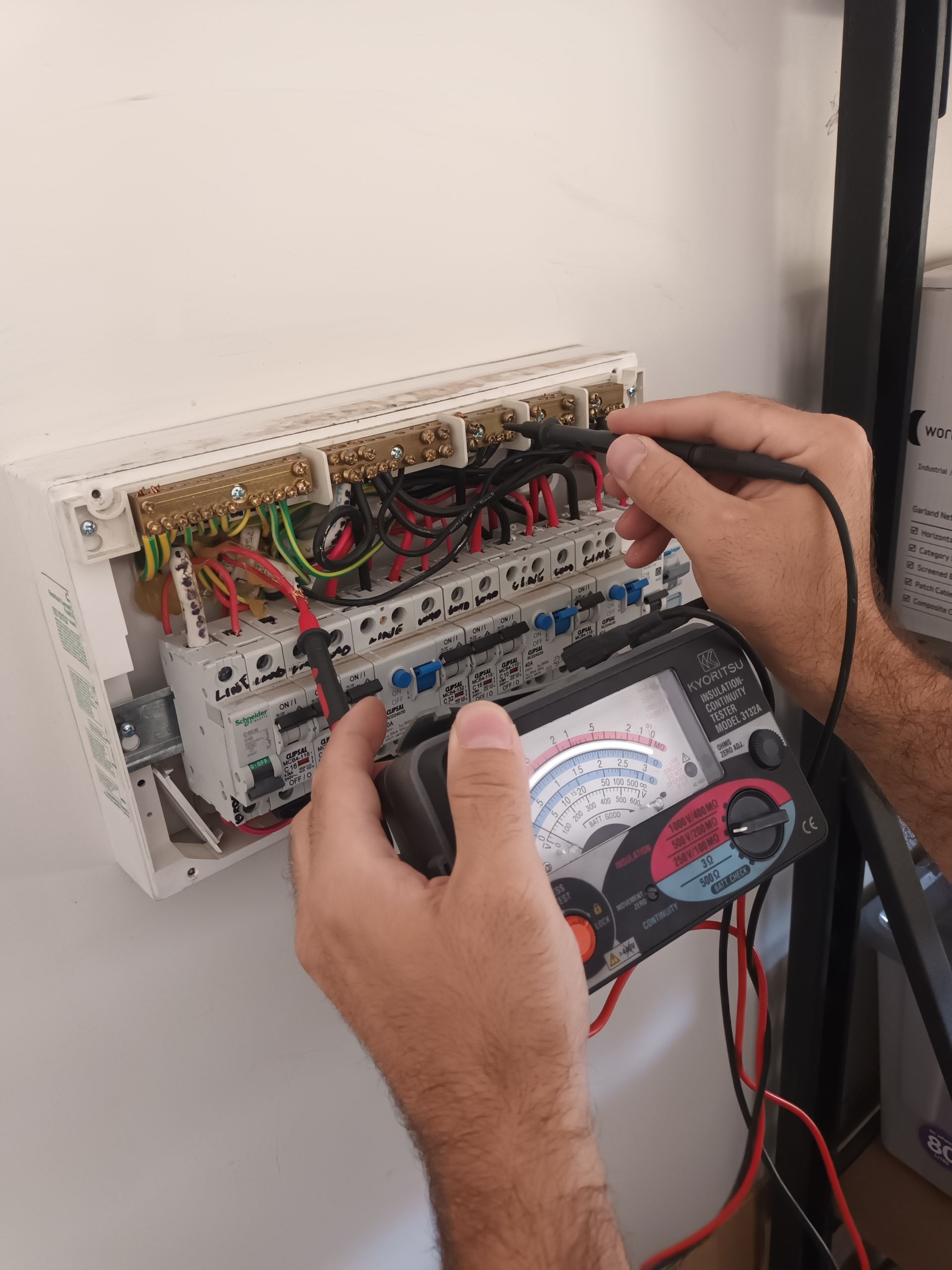 Person using a multimeter to test wires inside an electrical panel mounted on a white wall. — Ryphen Electrical in Highton, VIC