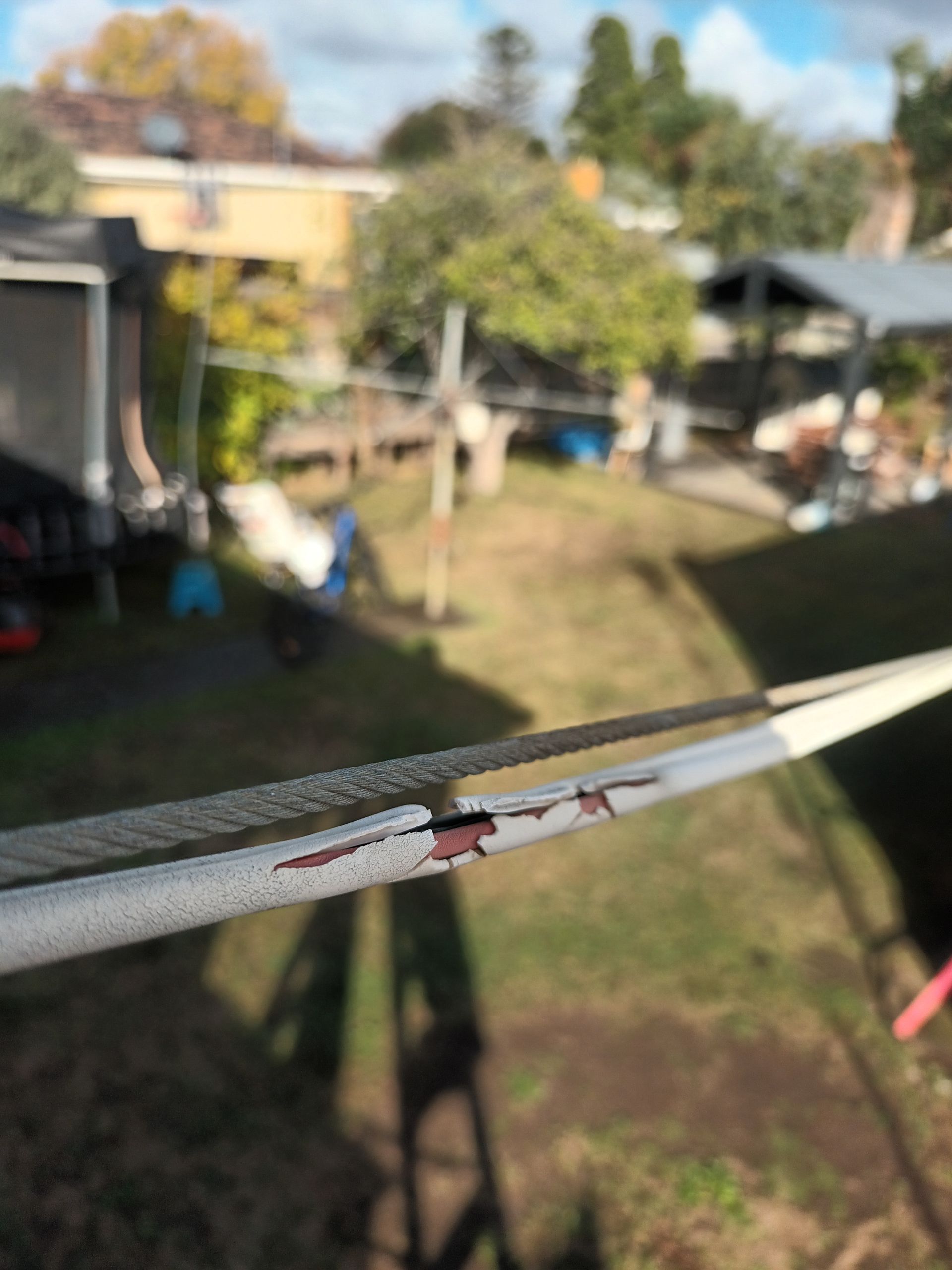 Close-up of damaged white clothesline with a break showing the inner material against a blurred backyard. — Ryphen Electrical in Highton, VIC