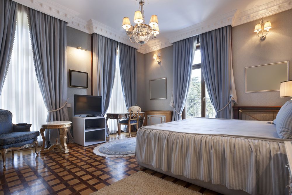 Elegant bedroom with blue curtains, chandelier, and bed with a ruffled skirt. — Ryphen Electrical in Highton, VIC