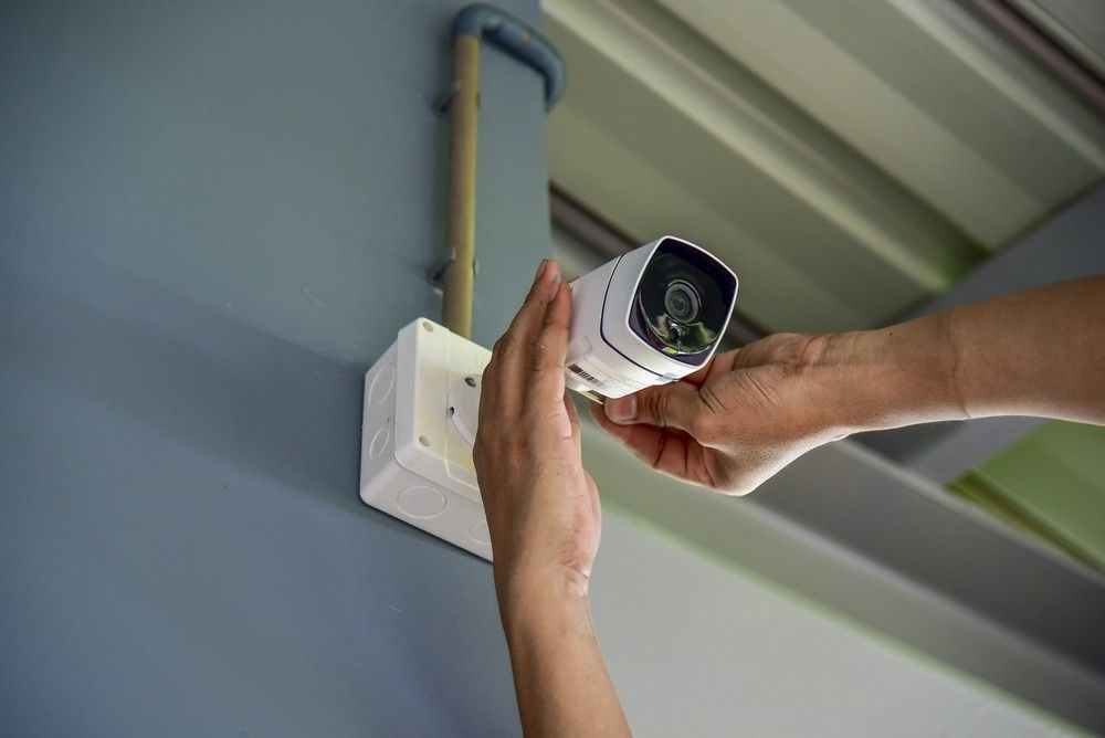 Hands Installing a White Security Camera on A Blue Wall — Ryphen Electrical in Highton, VIC