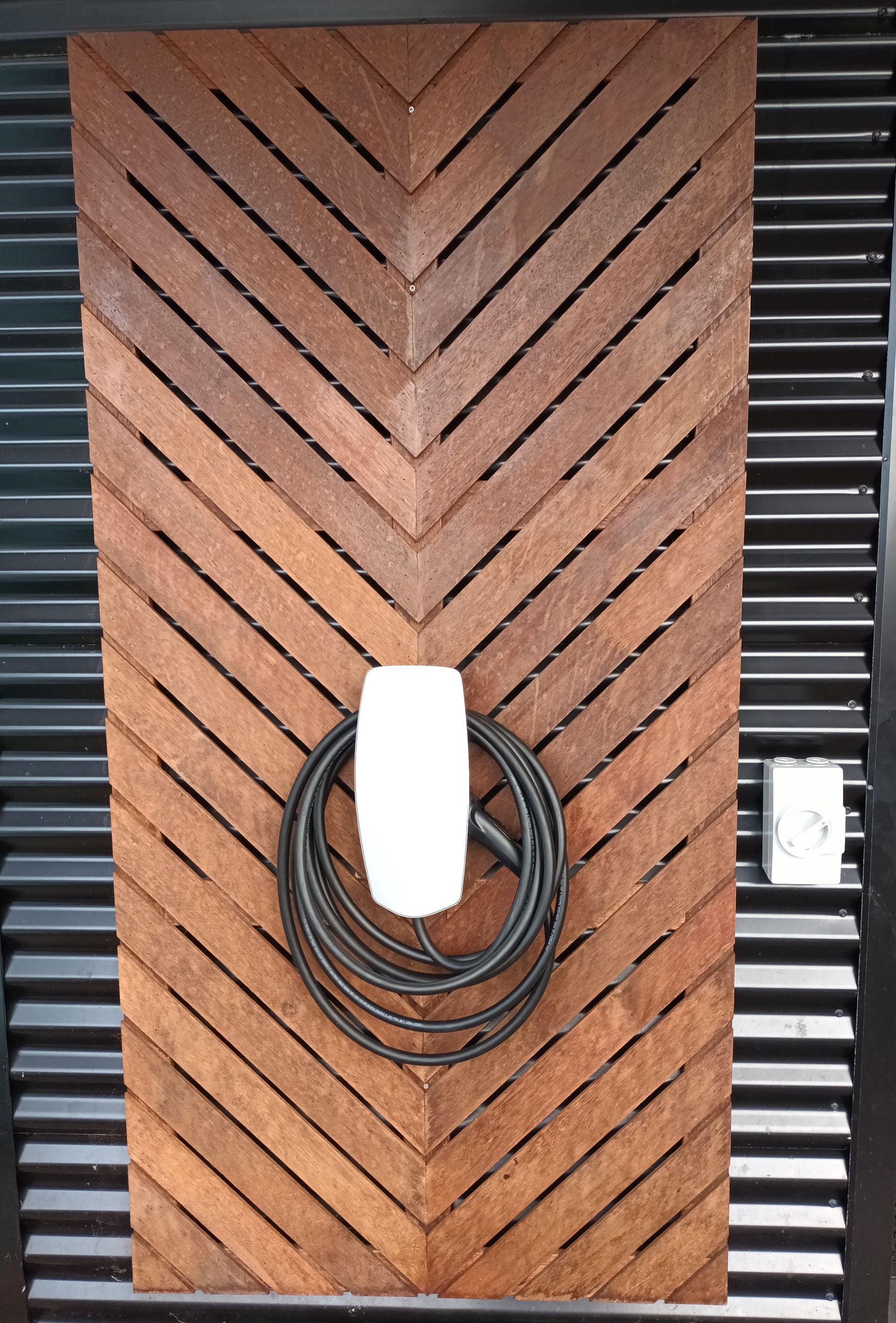 Wooden chevron wall with an electric car charger and coiled black cable. — Ryphen Electrical in Highton, VIC
