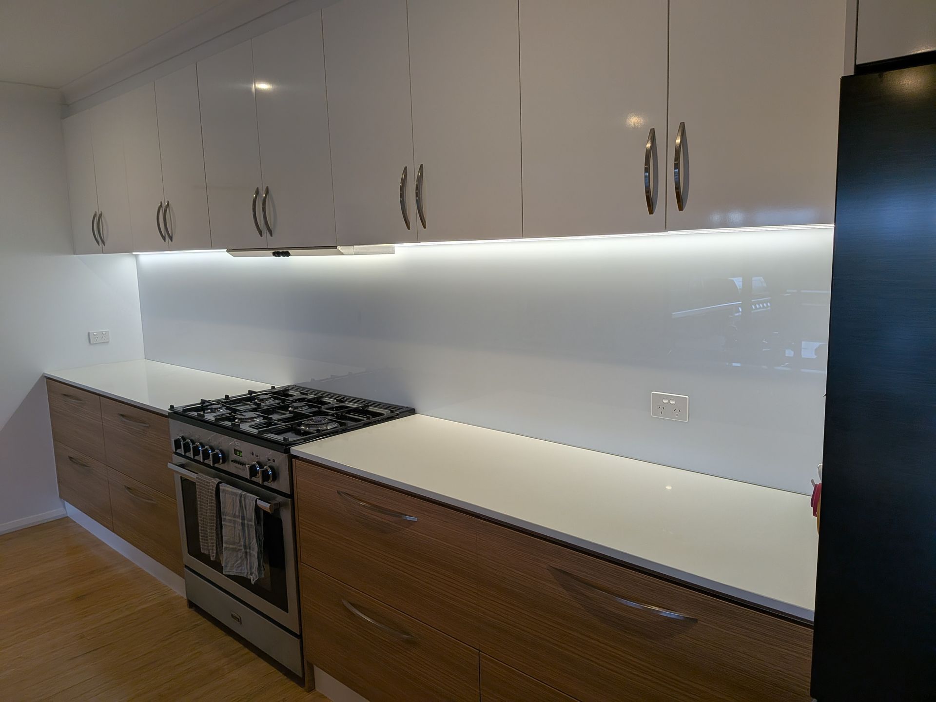 Modern kitchen with white upper cabinets, wood lower cabinets, and a gas range. — Ryphen Electrical in Highton, VIC