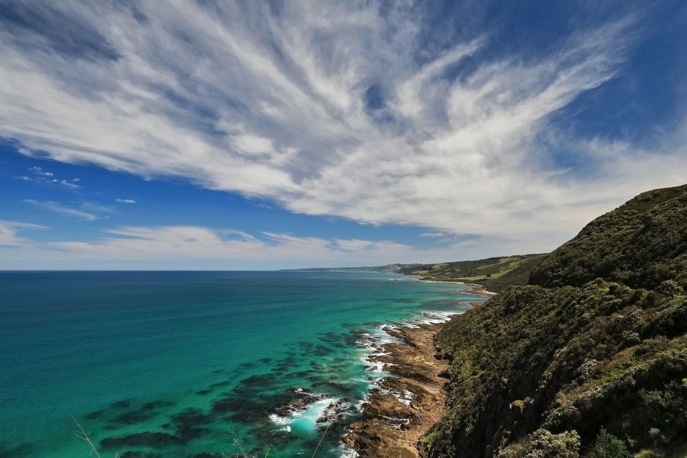 Azure Ocean Meets Rocky Coastline Under a Bright Blue Sky with Wispy Clouds — Ryphen Electrical in Colac, VIC