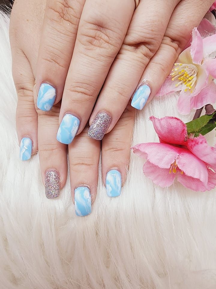 A woman's nails are painted blue and silver and sit next to a pink flower.