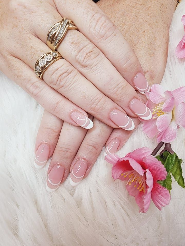 A close up of a woman 's hands with rings and french manicure.