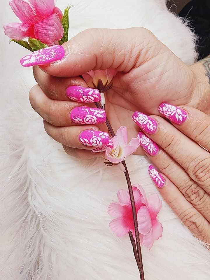 A woman's hand with long pink nails is holding a pink flower.