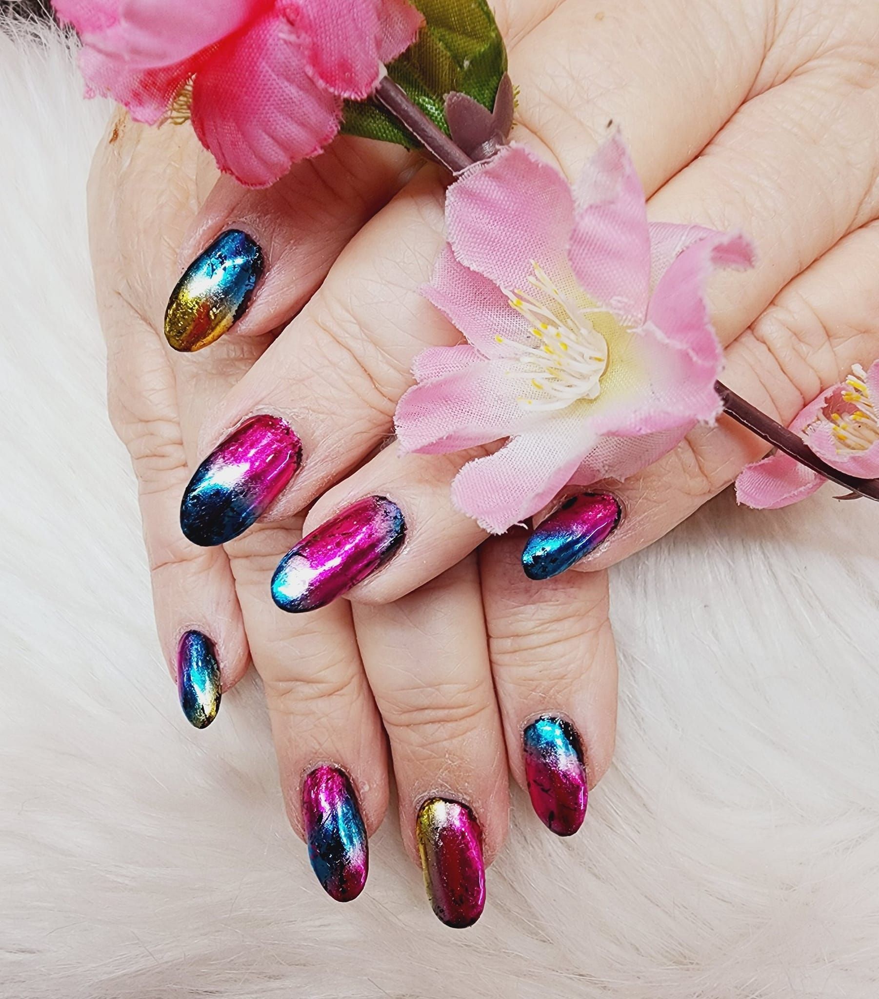 Nails are painted in different colors, and she is holding a pink flower.