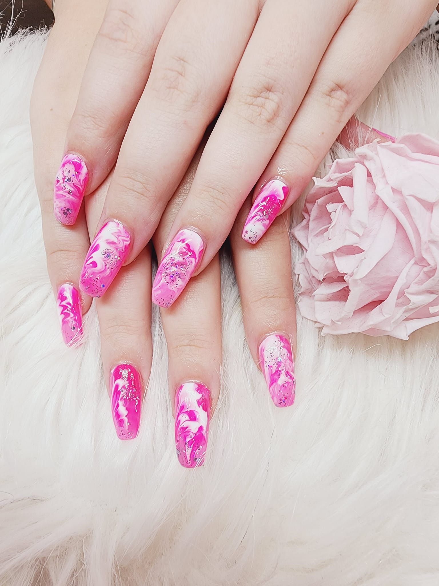 A woman's nails are painted pink and white, and she is holding a pink rose.