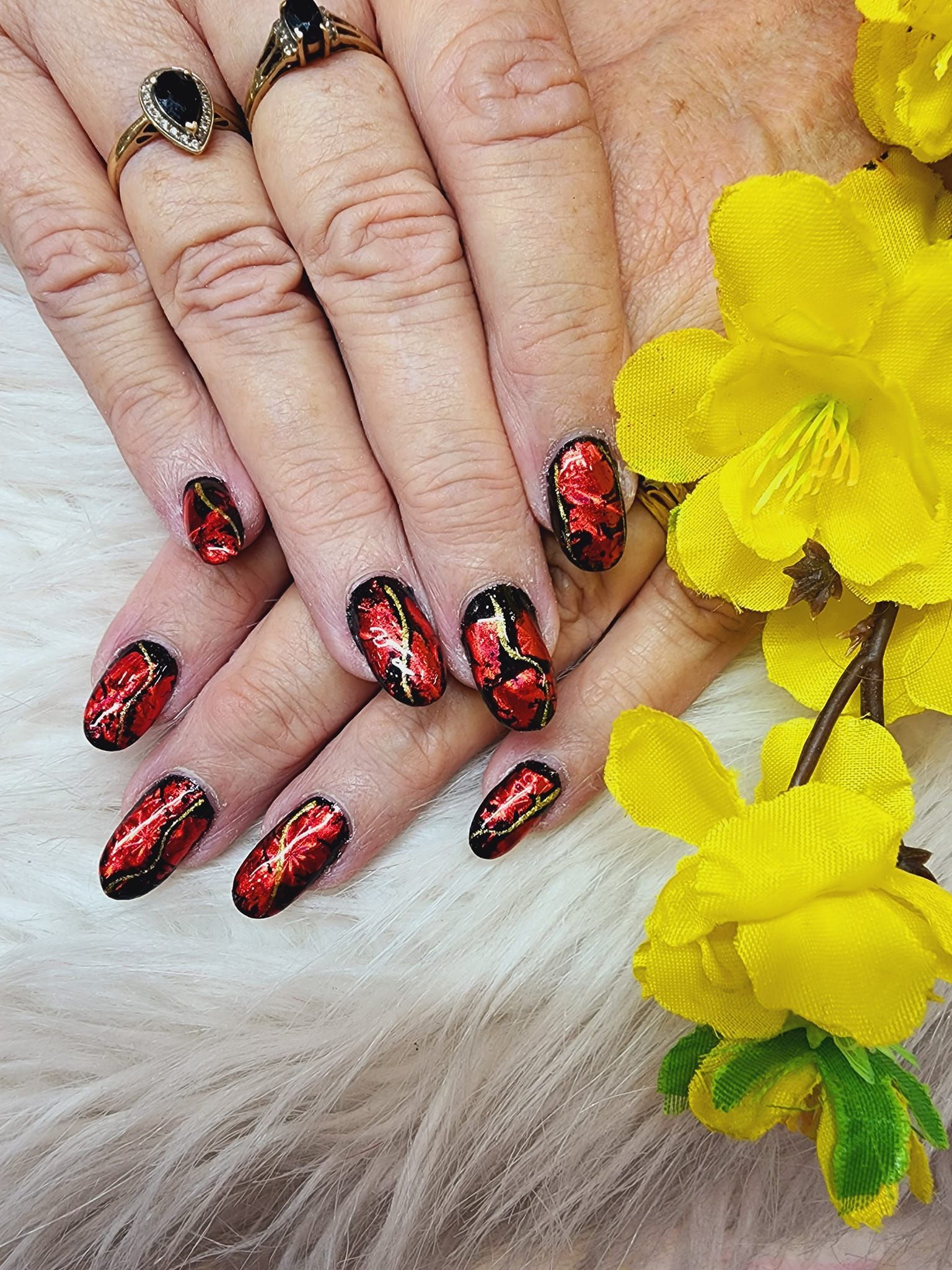 A close up of a woman 's nails with red and black designs and a yellow flower.