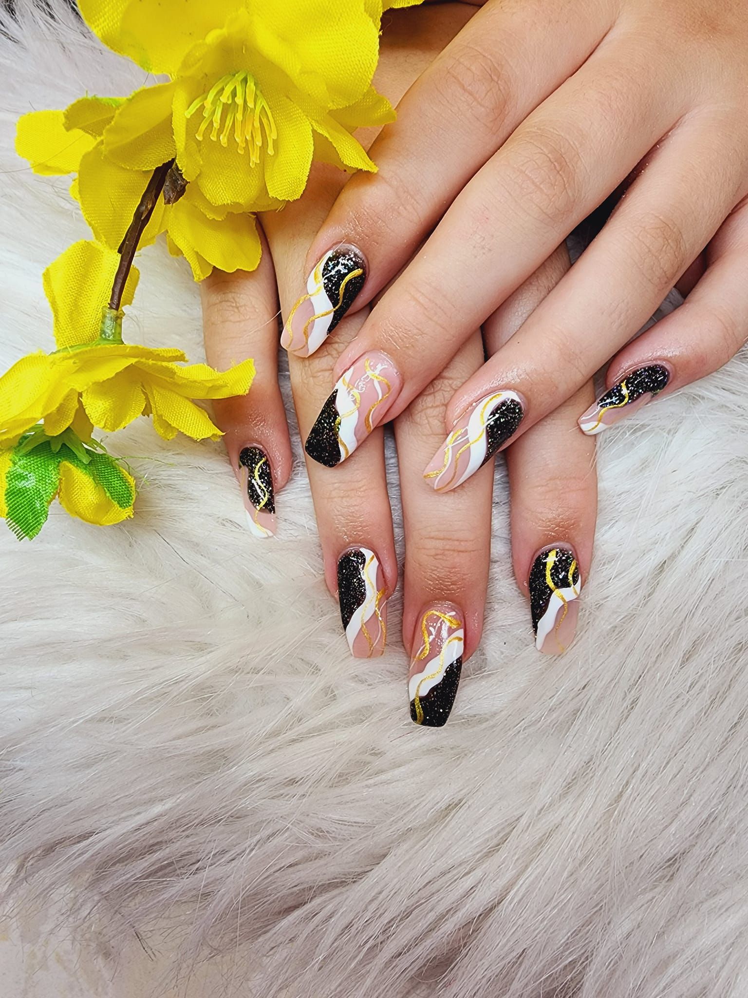A close-up of a woman's nails with a yellow flower in the background.