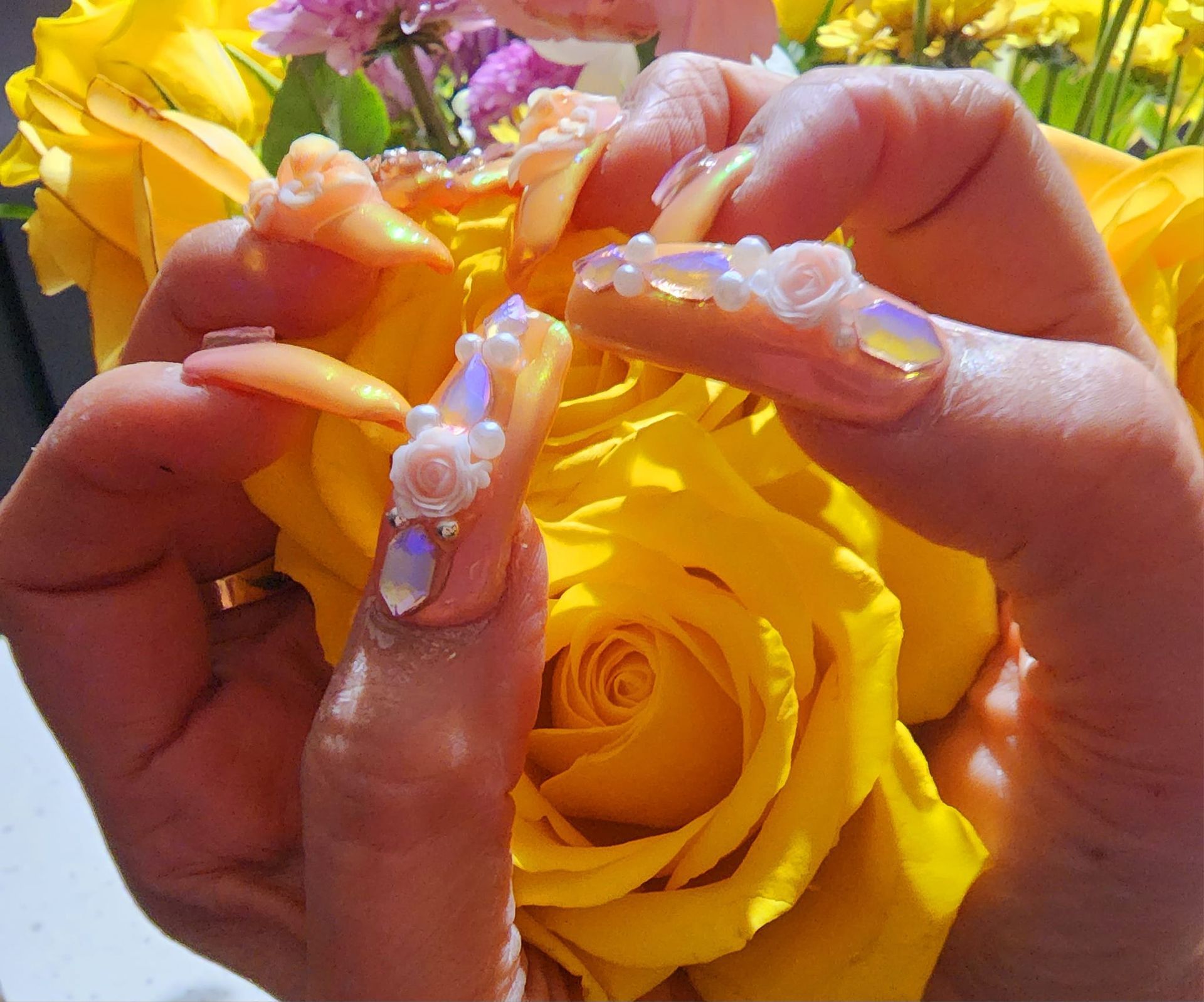 A woman with long nails is holding a yellow rose.