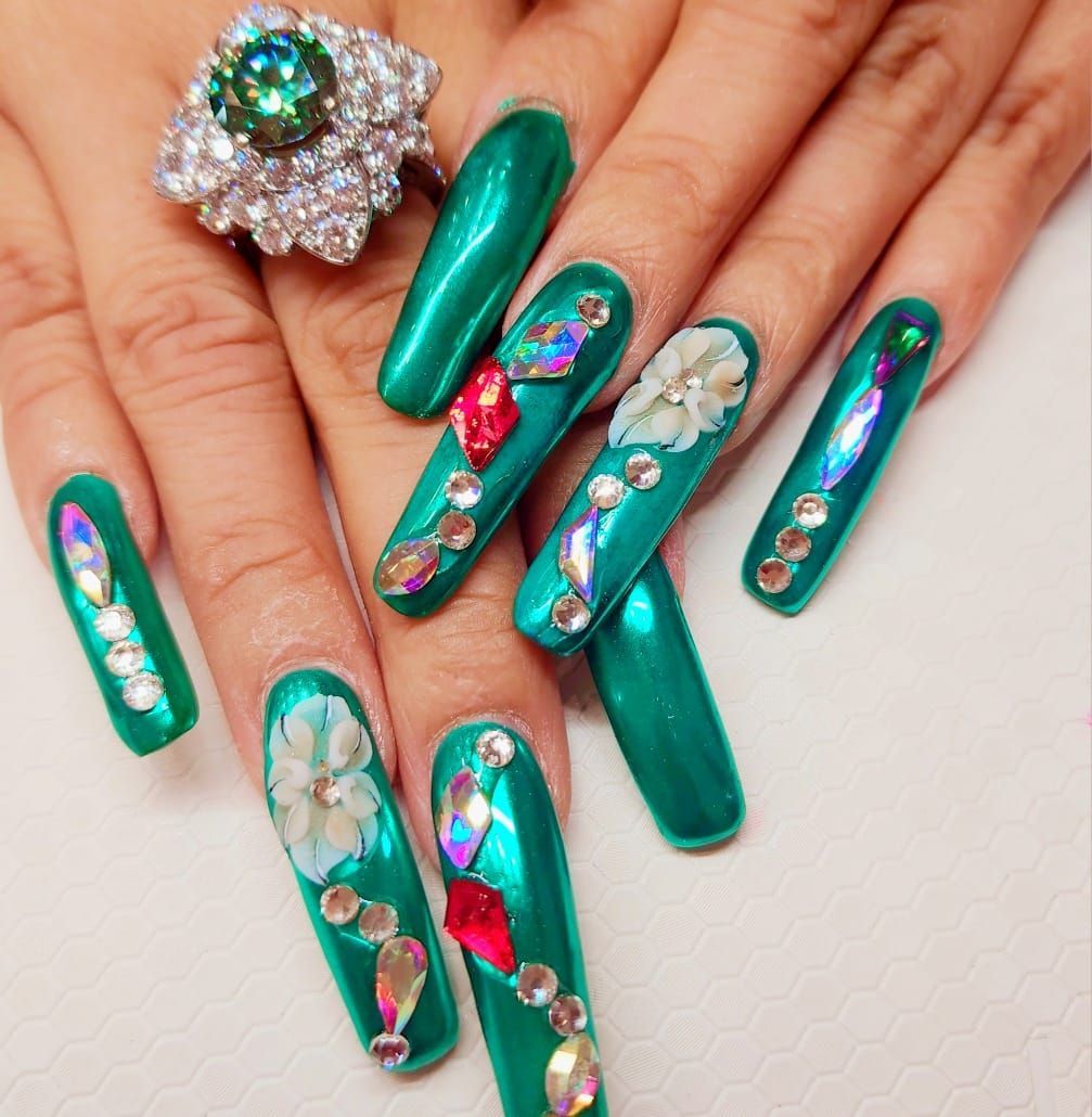 A woman's hand with long green nails and a ring on her finger.
