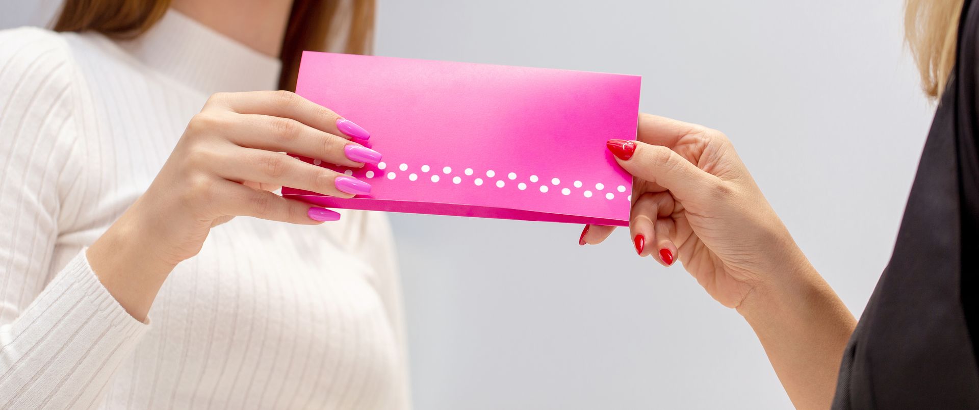 A woman is giving a pink envelope to another woman.