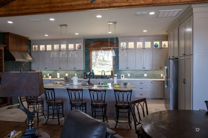 Modern kitchen with island, bar stools, white cabinets, and stainless steel refrigerator beneath wood ceiling