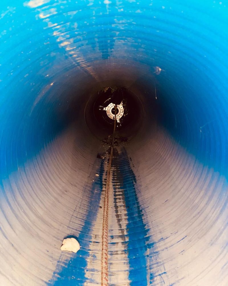 Vista interna di un grande tunnel blu e grigio, con un'apertura scura in fondo e un piccolo oggetto appeso in cima.