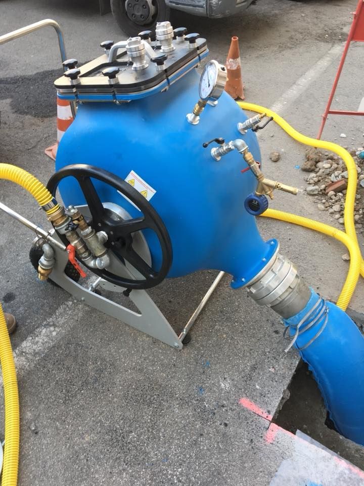 Macchina di intercettazione dell'acqua blu con tubi flessibili, installata su una strada accanto a un pozzo di servizio aperto.