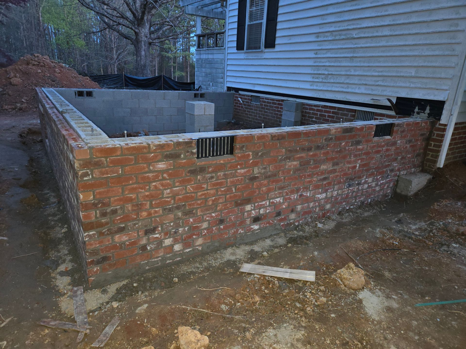 A newly constructed red brick foundation wall for a home addition, featuring exposed gray concrete blocks and vents.