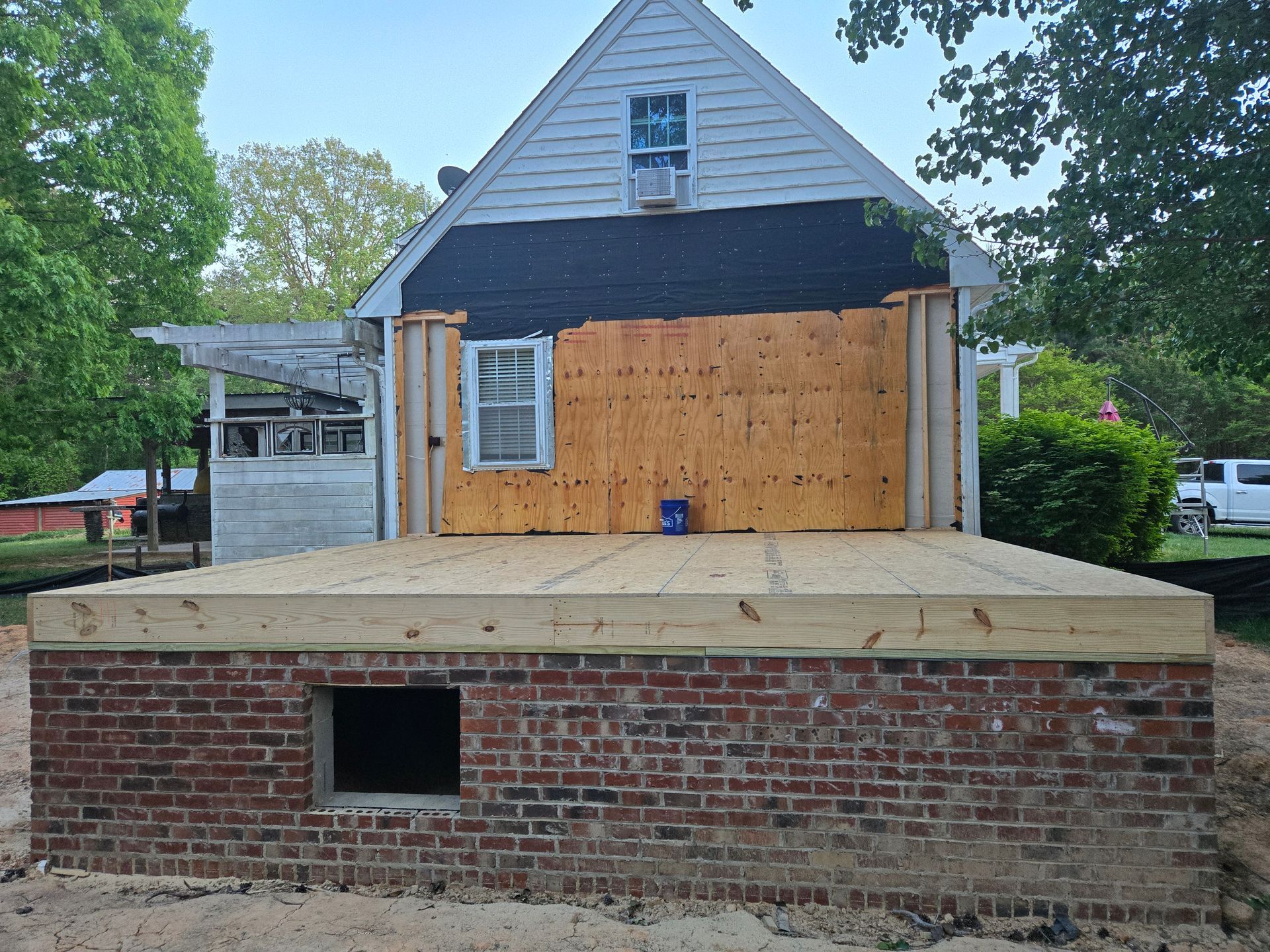 A house addition under construction with a new wooden deck platform built over a brick foundation.