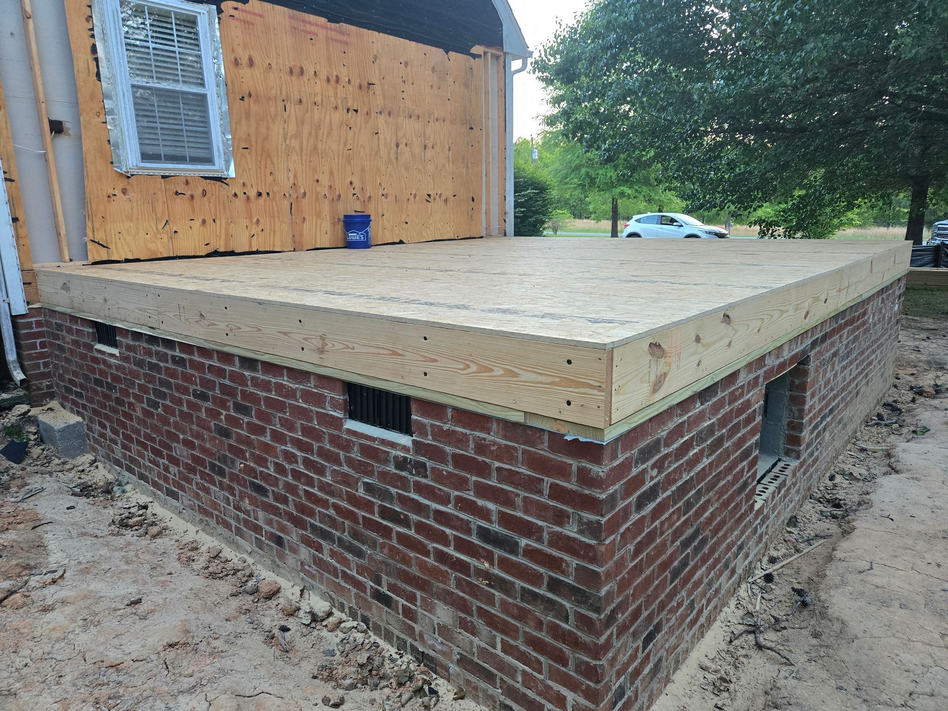 A brick foundation wall with a newly installed wooden subfloor and plywood wall sheathing under construction.