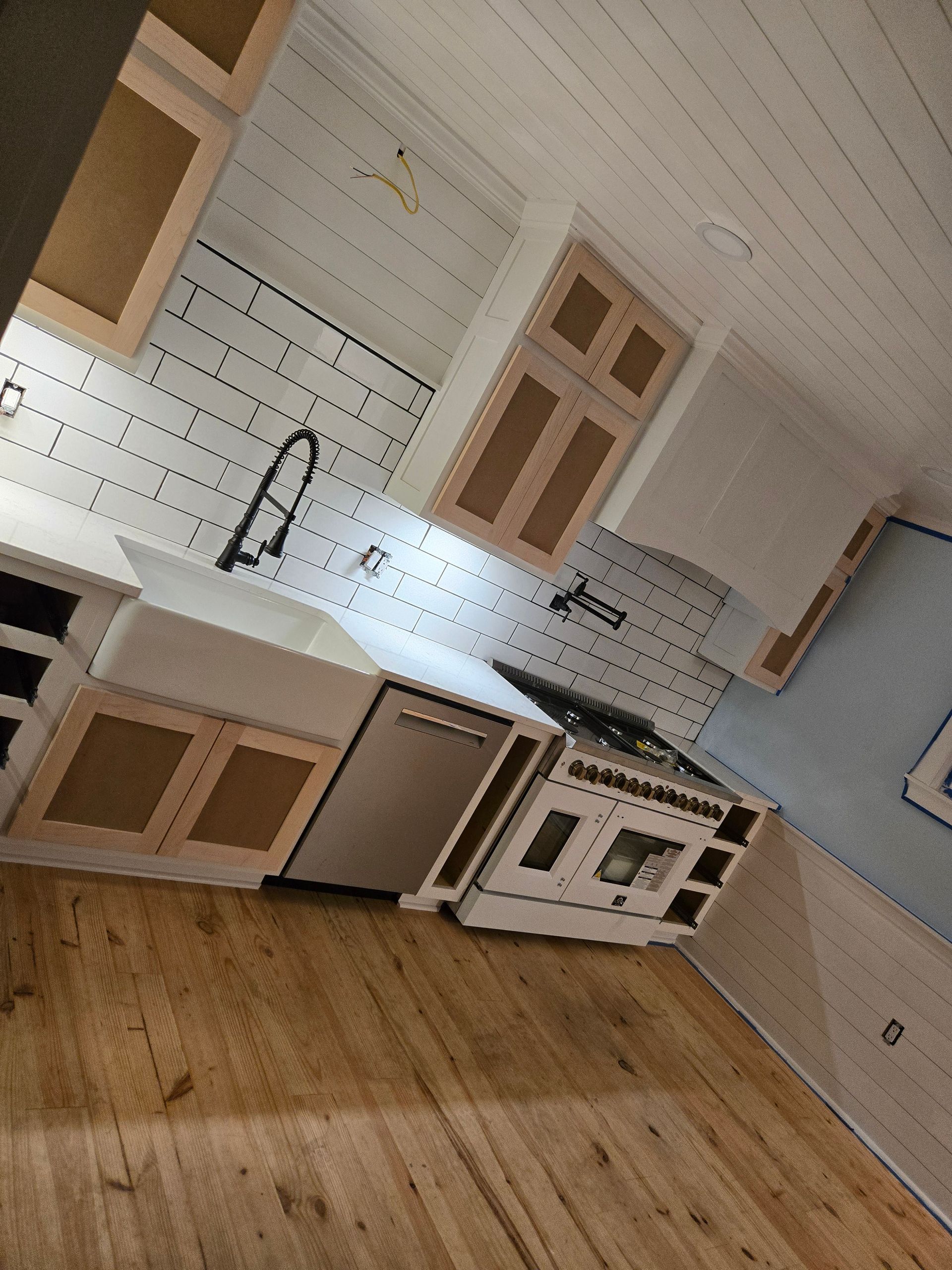 A kitchen with white subway tile, a farmhouse sink, stainless steel dishwasher, white range, and wood-toned cabinets.