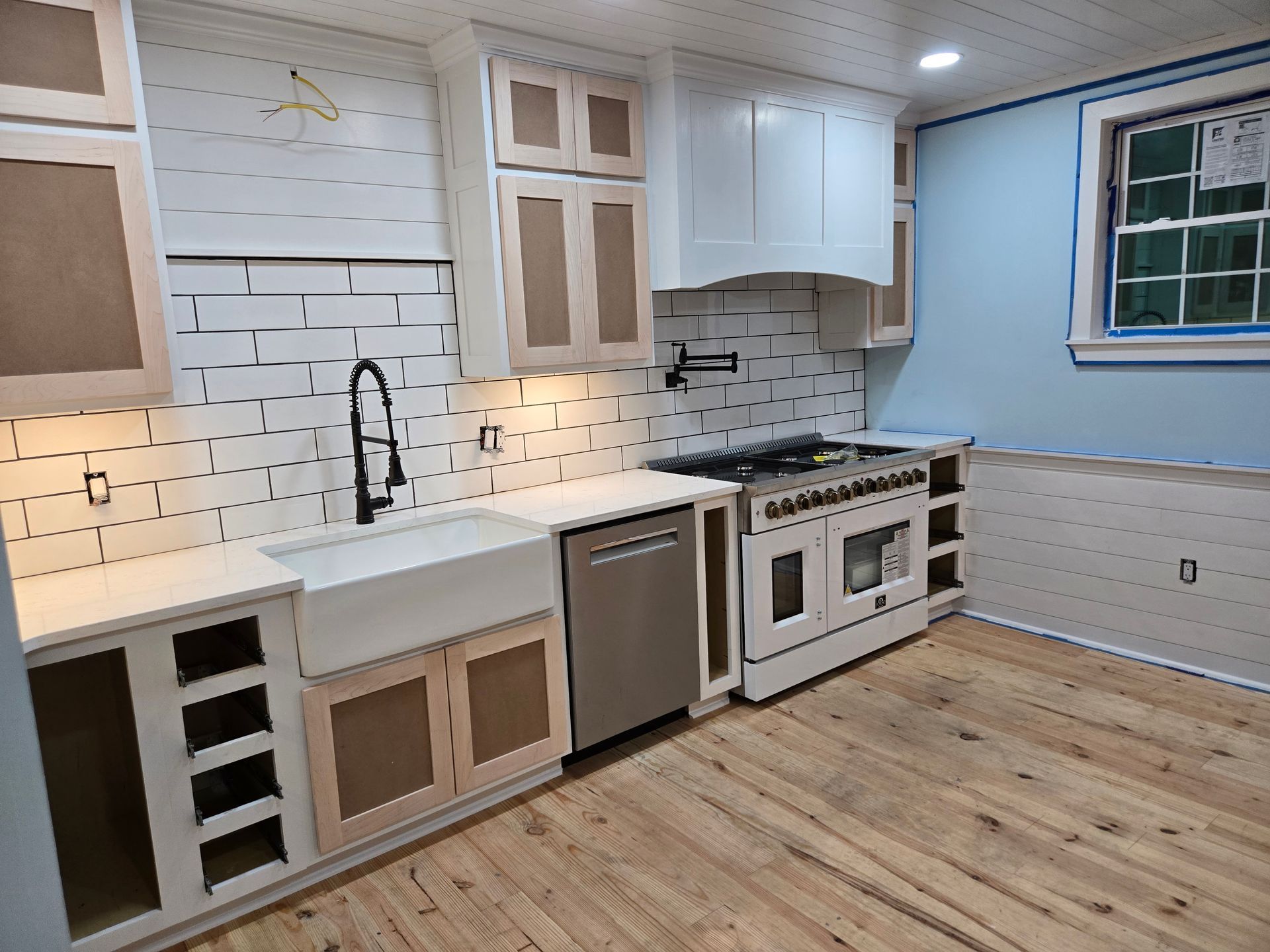 A kitchen under construction with white cabinets, a farm sink, stainless steel appliances, and unfinished subway tile.