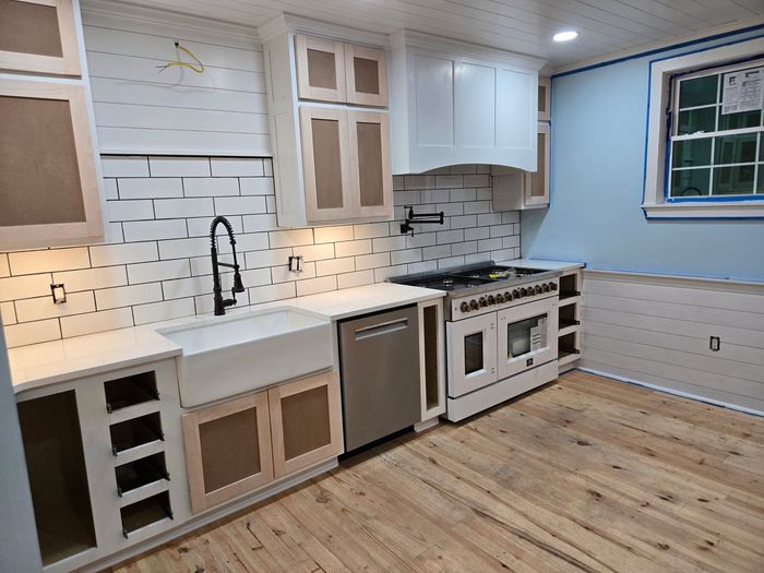 A kitchen under construction with white cabinets, a farm sink, stainless steel appliances, and unfinished subway tile.