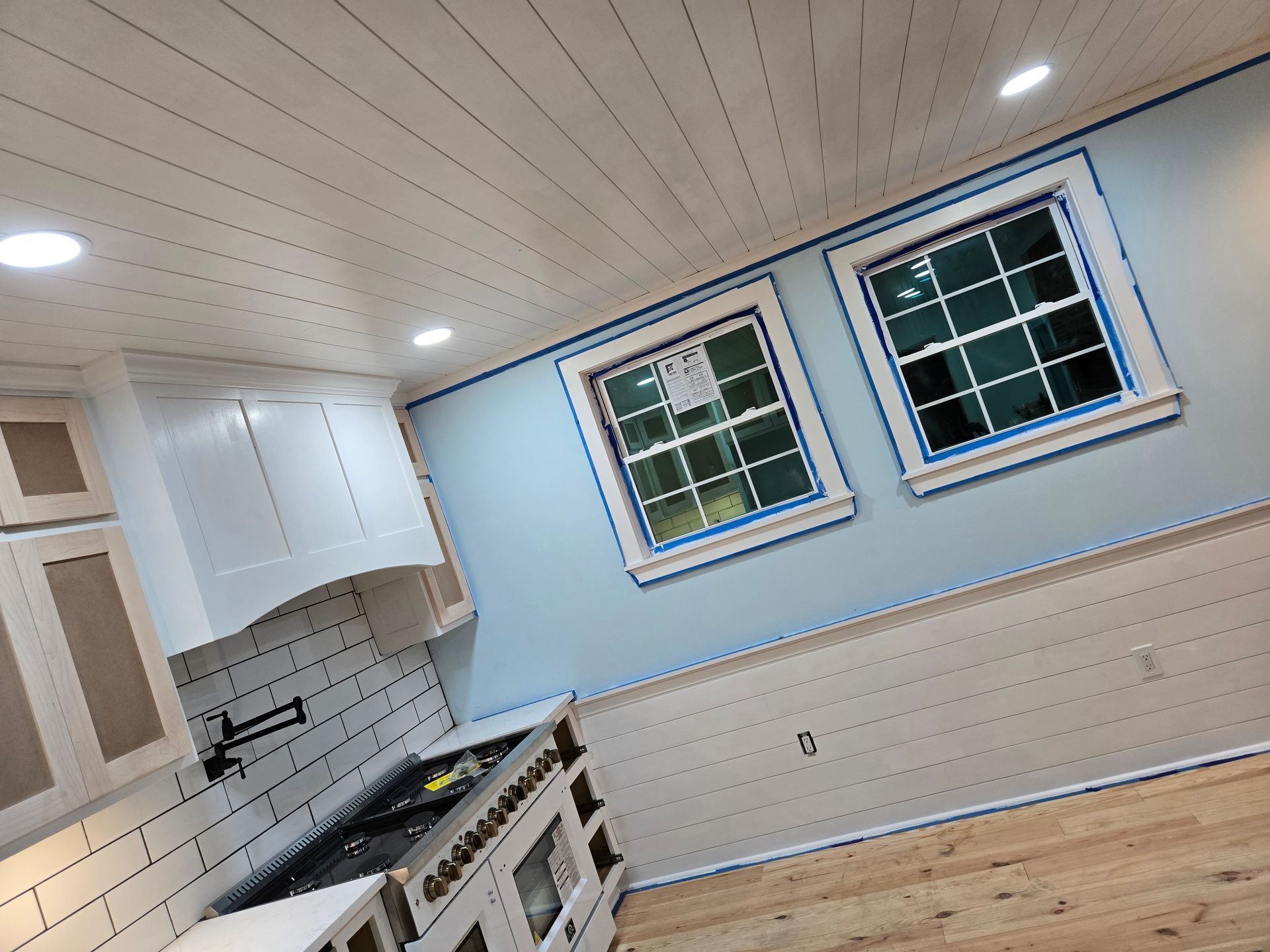 A kitchen featuring light blue walls, white shiplap wainscoting and ceiling, white cabinets, a subway tile backsplash.