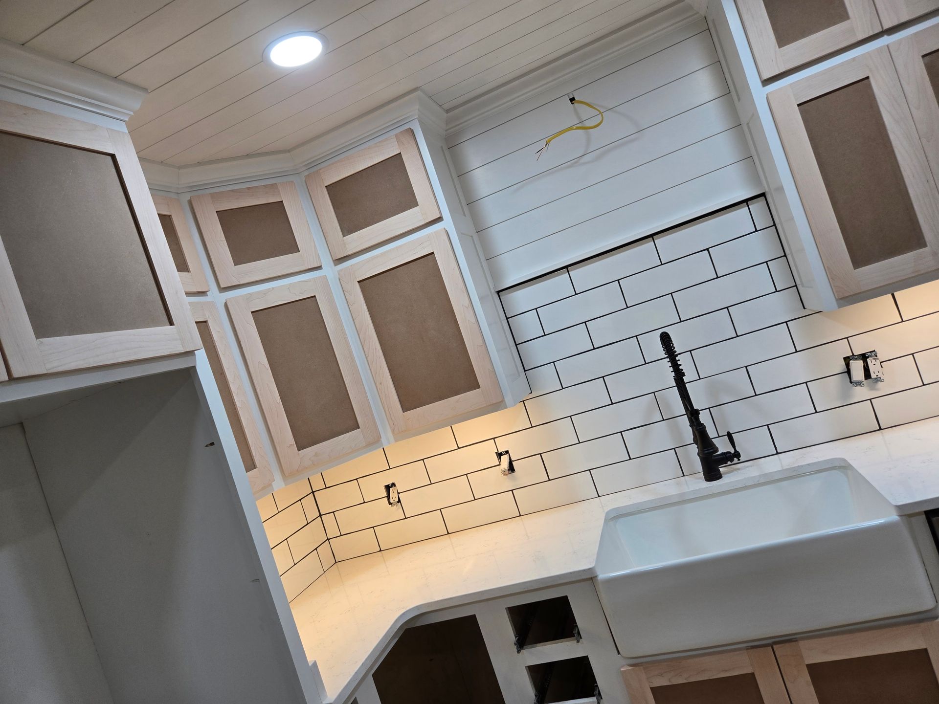 A modern kitchen under construction with white shaker cabinets, white subway tile backsplash, and a farmhouse sink.