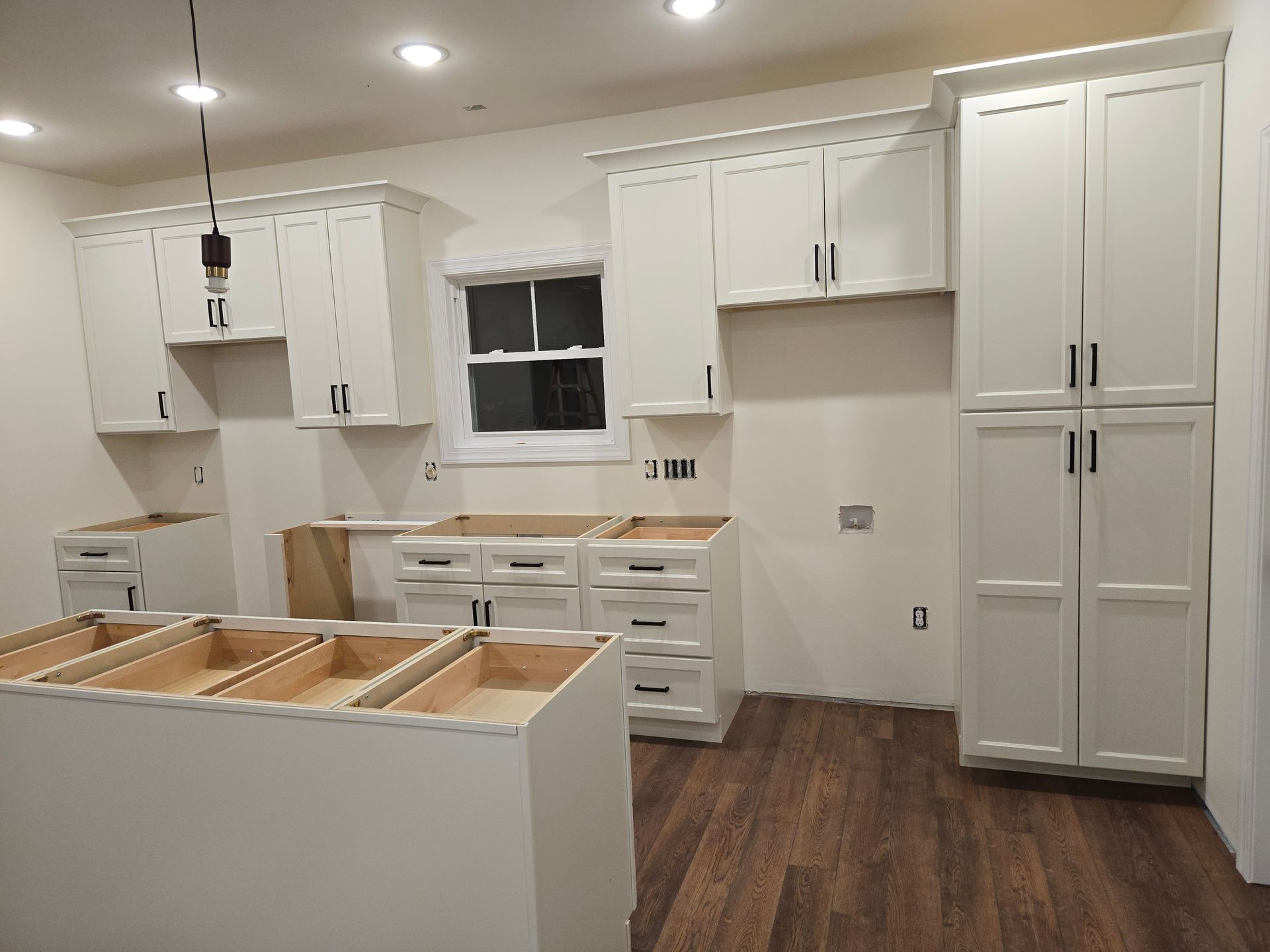 A modern kitchen under renovation with white cabinets, a central island, and dark wood flooring.