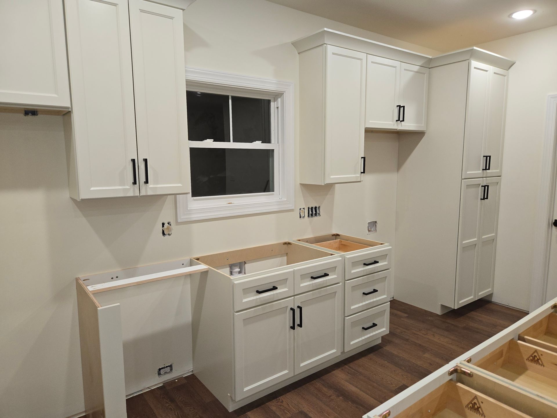 White kitchen cabinets and drawers installed in a room with wood-look flooring and a window.