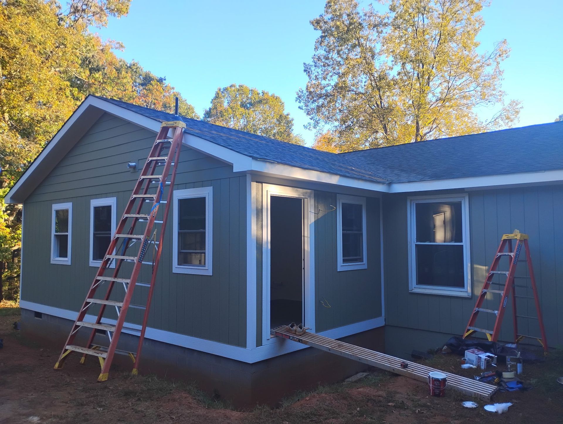 A green-sided house under renovation with two ladders leaning against the exterior walls and a small deck entryway.