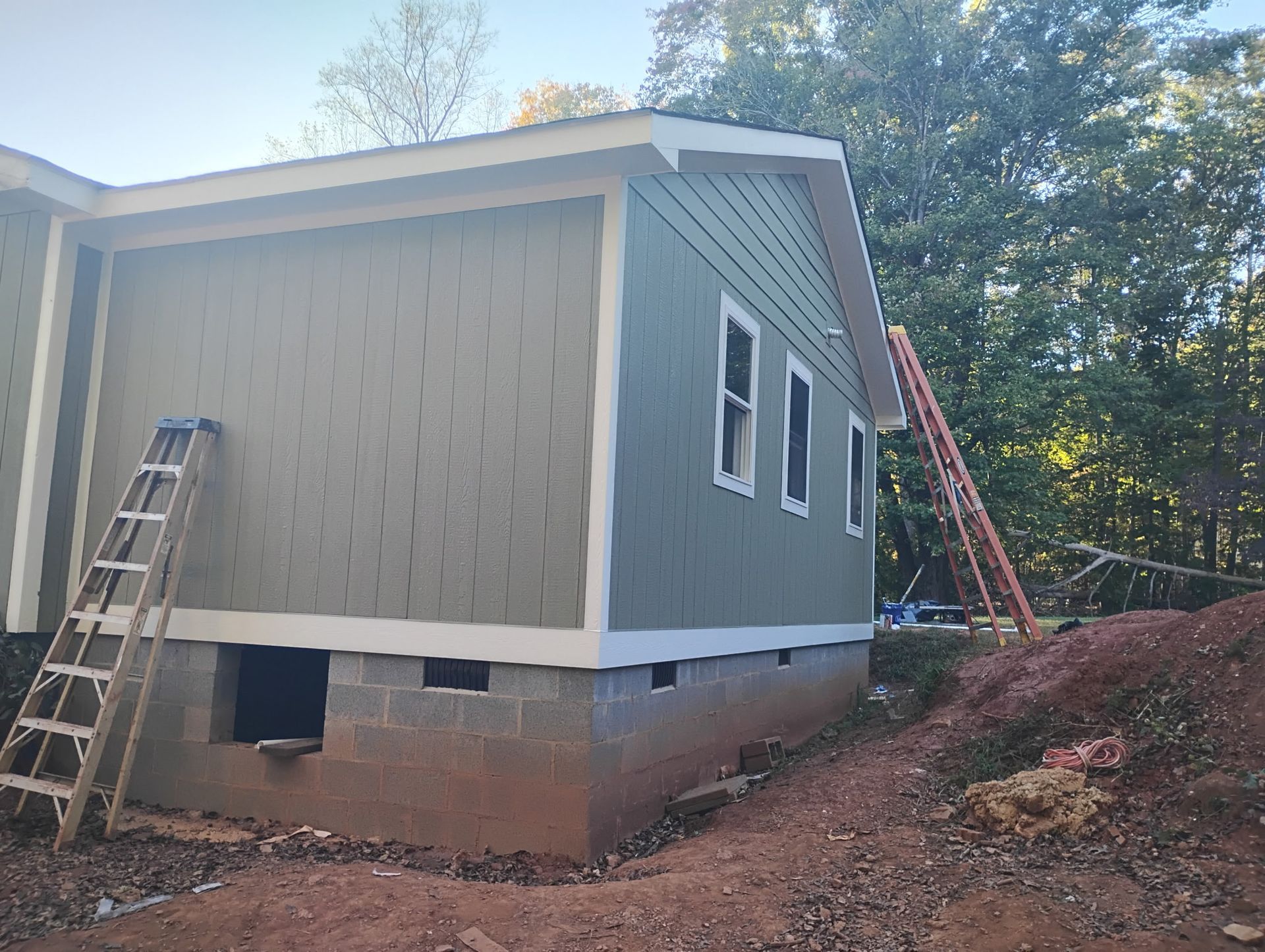 A side view of a house under construction with light green siding, white trim, and a ladder leaning against the wall.