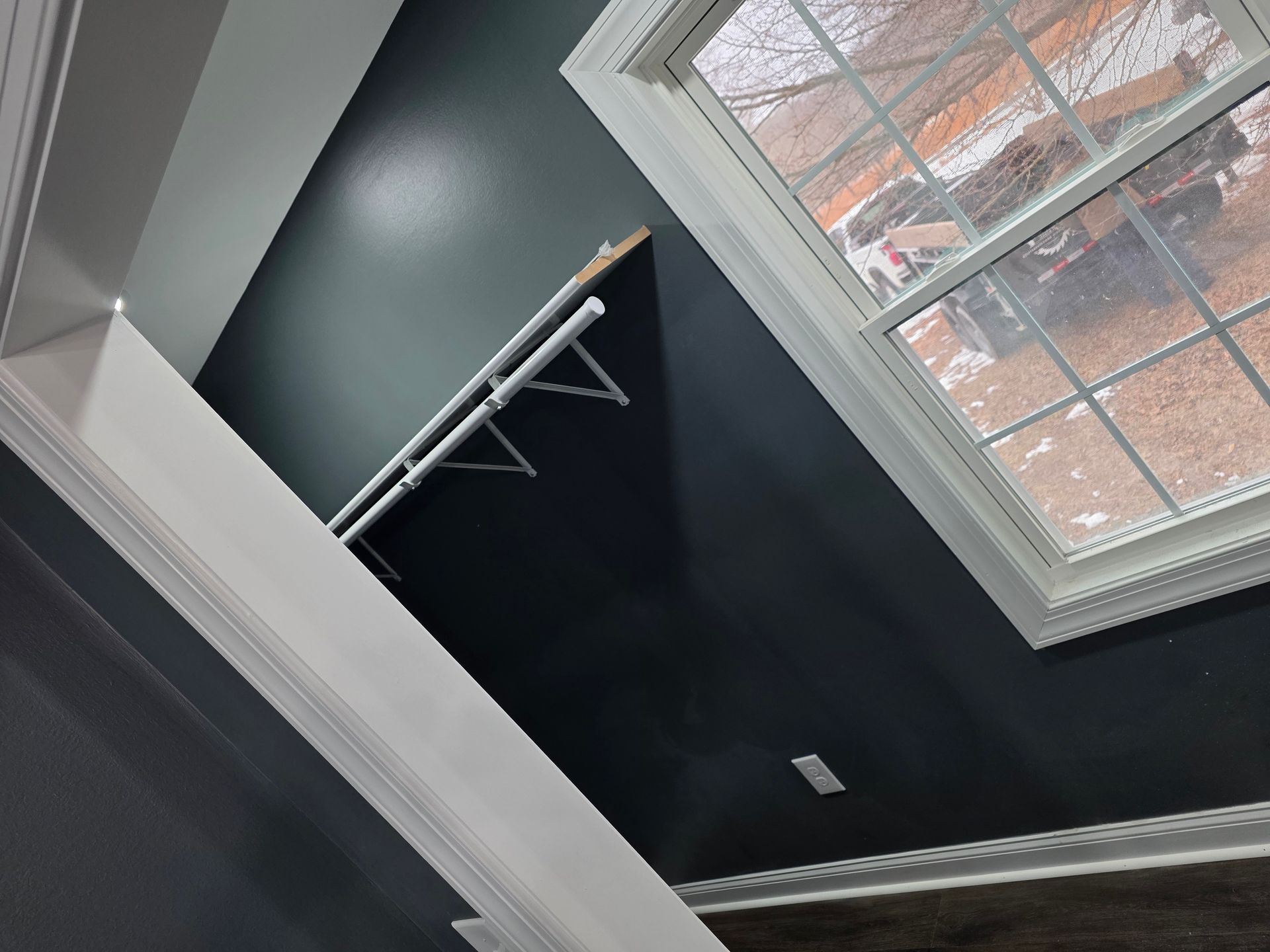 A low-angle view of a room with dark charcoal walls, white trim, a window, and a white wall-mounted shelf with brackets.