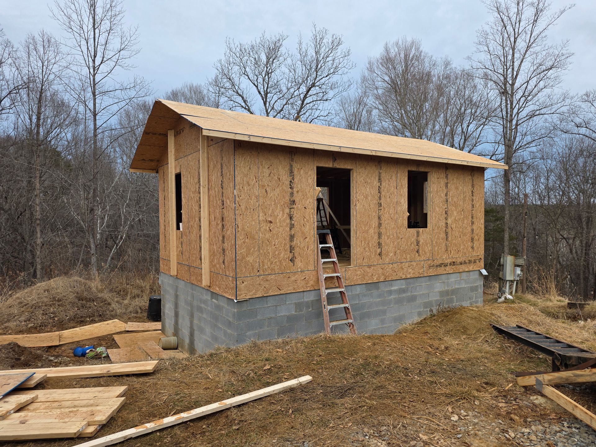 A wooden shed under construction with an OSB-paneled frame on a concrete block foundation outdoors under a cloudy sky.