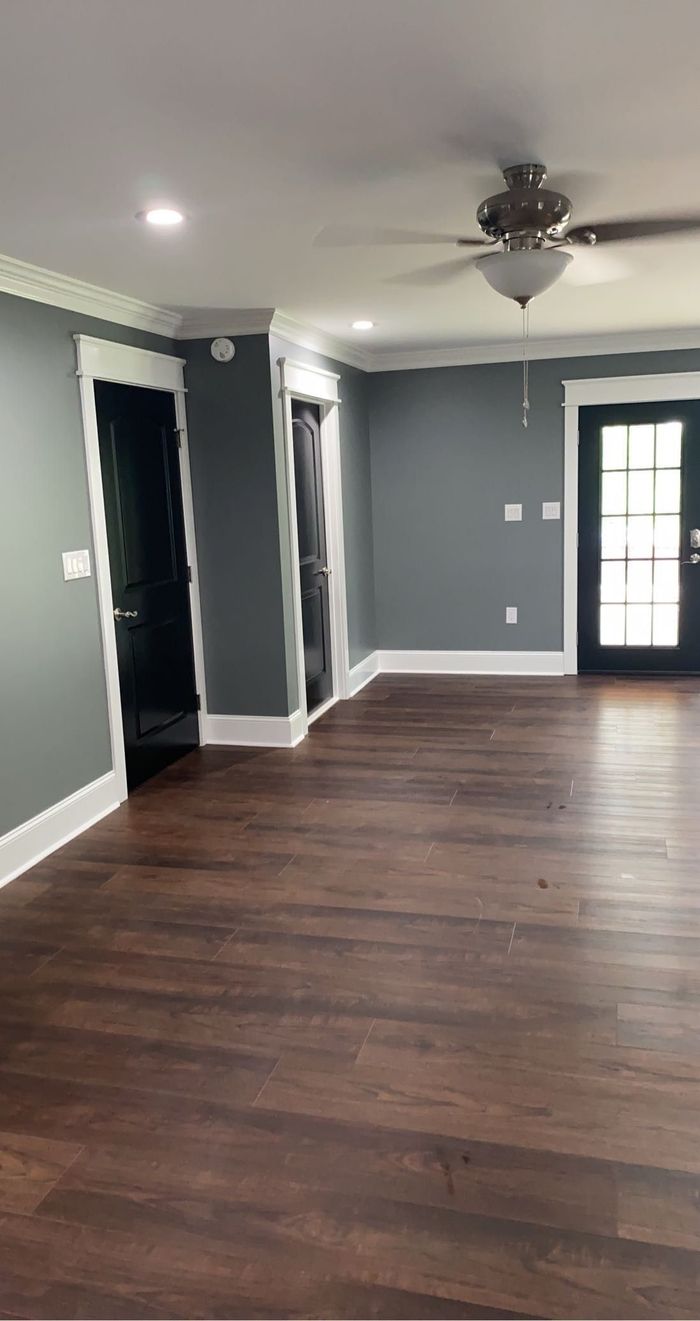 A bright, empty room with dark gray walls, white trim, dark hardwood floors, and a ceiling fan.