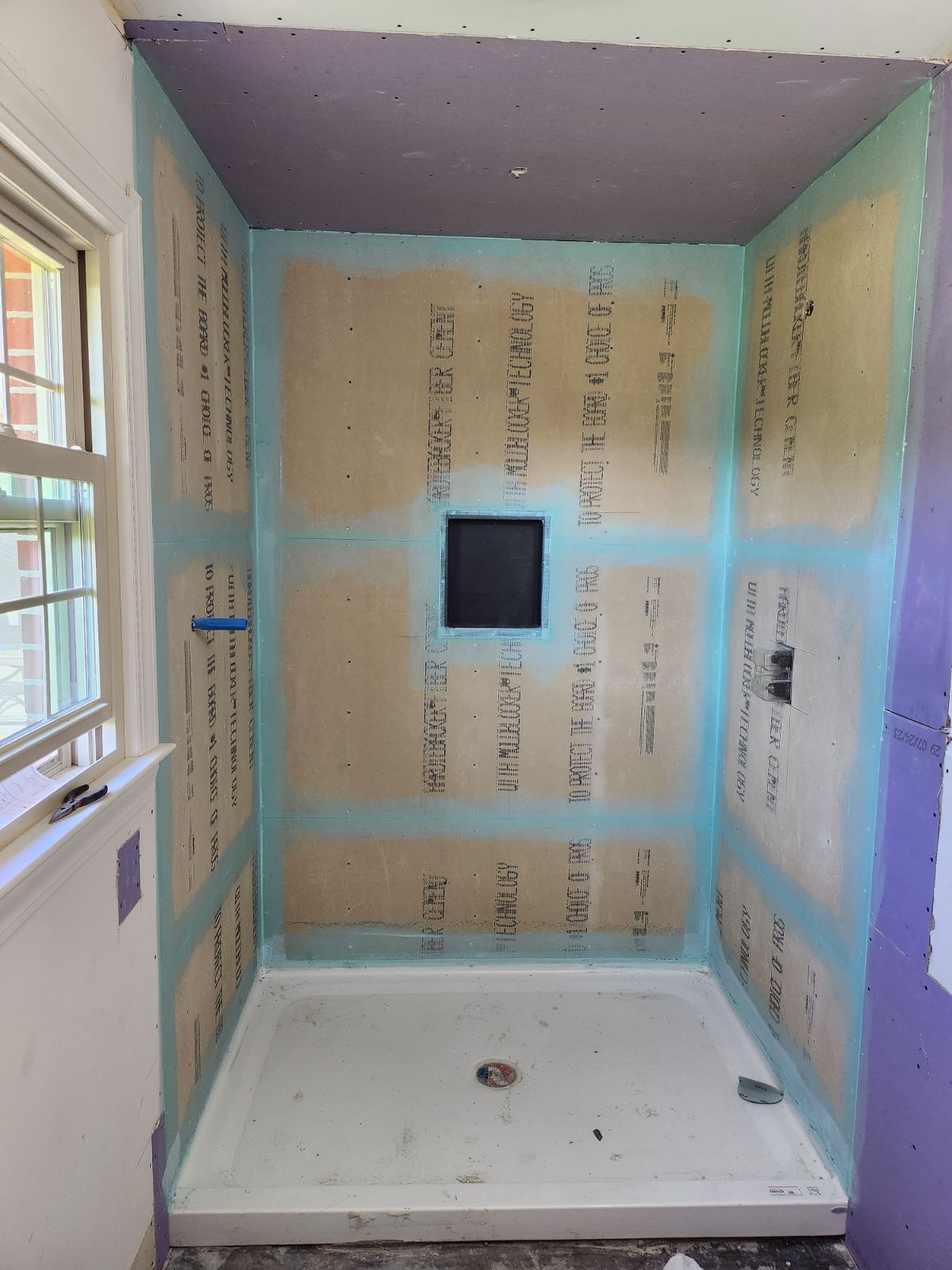 A shower alcove under construction with cement board walls, blue waterproof seams, a recessed niche, and a shower pan.
