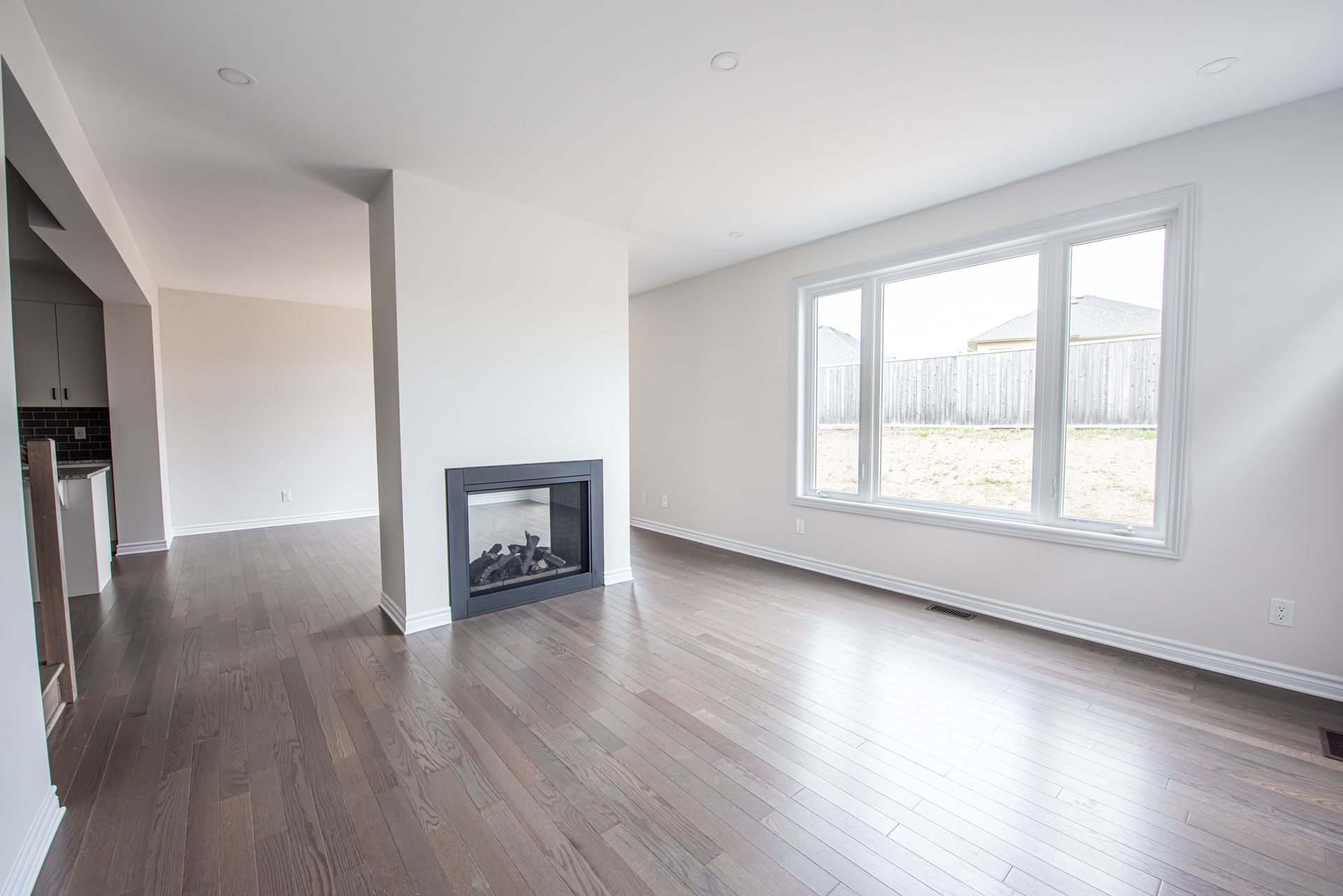 A bright, empty living room with dark hardwood floors.