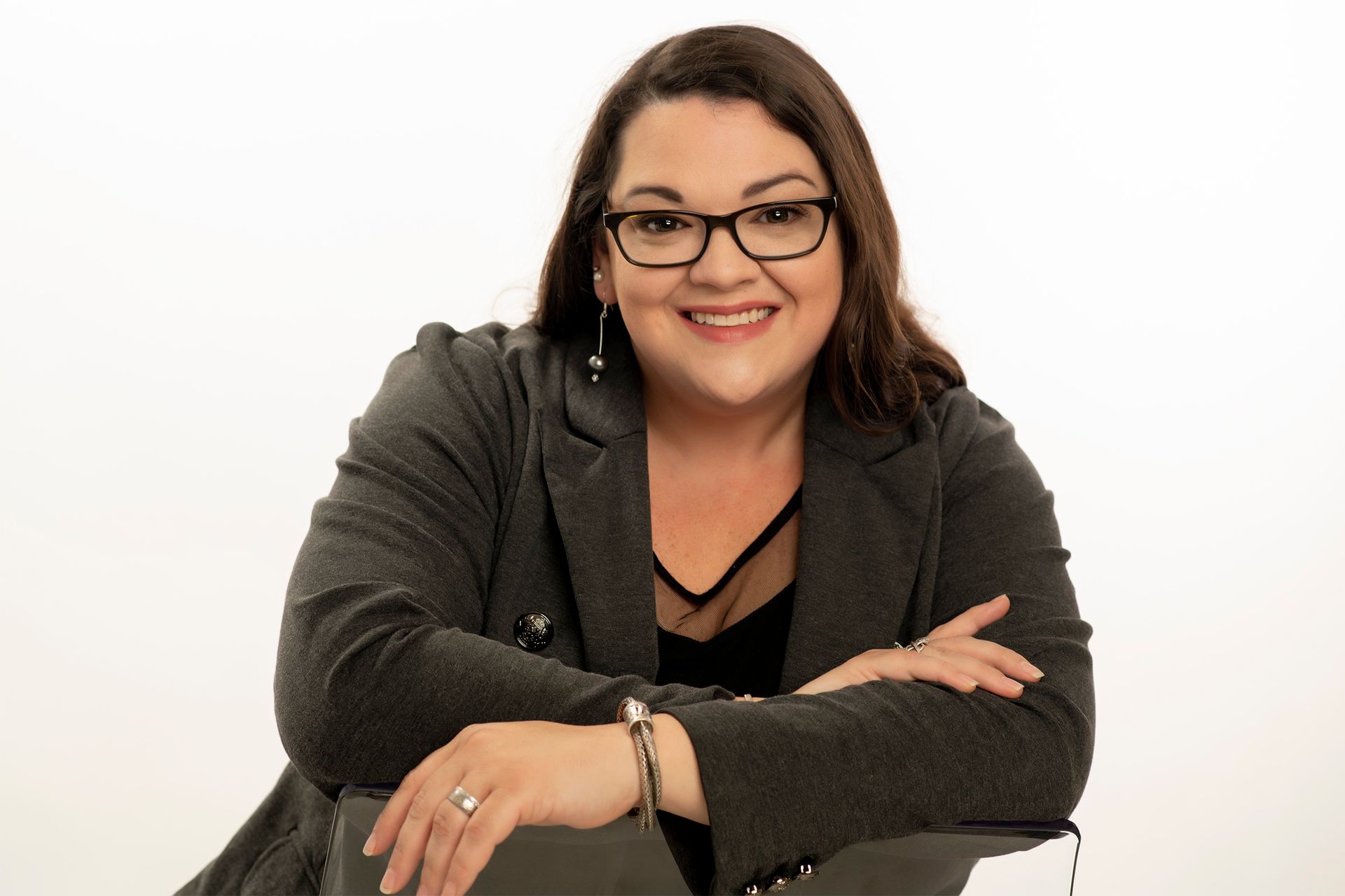 A woman wearing glasses and a gray jacket is sitting at a table with her arms crossed.